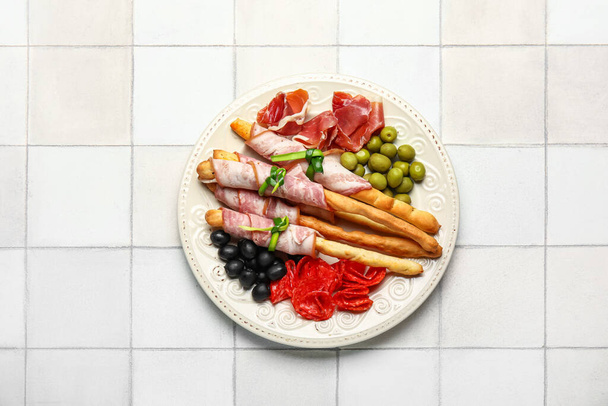 Plate of tasty Italian Grissini with bacon on white tile background - Foto, Bild