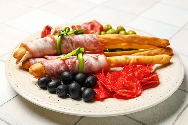 Тарелка вкусного итальянского гриссини с беконом на белом кафельном фоне, крупный план - Фото, изображение