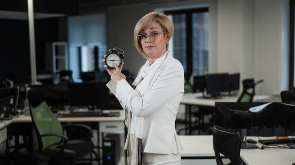 Caucasian business woman pointing on alarm clock in office - Foto, Bild