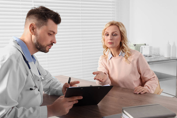 Doctor with clipboard consulting patient at table in clinic - Foto, Imagem