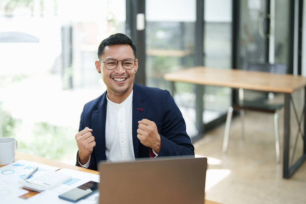Retrato de um empresário asiático do sexo masculino em pé com um computador mostrando felicidade após um investimento bem sucedido. - Foto, Imagem