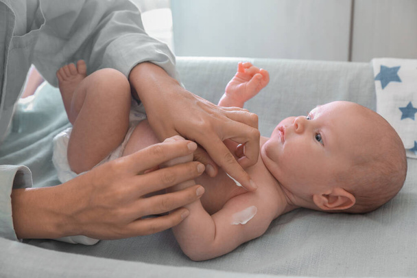 Mother applying moisturizing cream onto baby`s arm on changing table indoors, closeup - Fotoğraf, Görsel