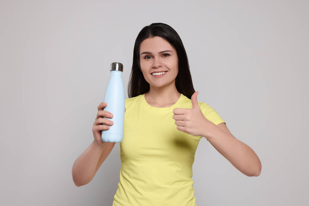 Young woman with thermo bottle on light grey background - Photo, image