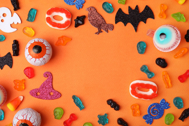 Frame made of tasty candies and Halloween decorations on orange background, flat lay. Space for text - Fotoğraf, Görsel