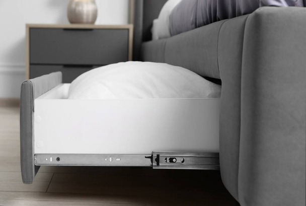 Storage drawer with white pillow under modern bed in room - Fotoğraf, Görsel