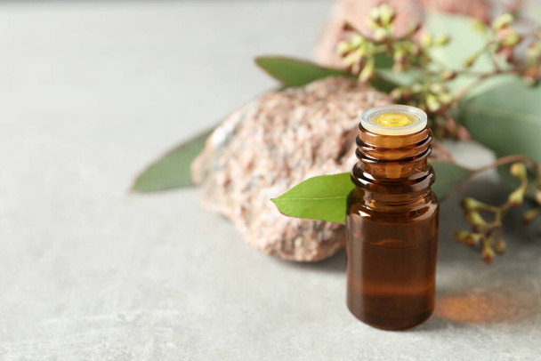 Bottle of eucalyptus essential oil, stone and leaves on light grey table. Space for text - Photo, image