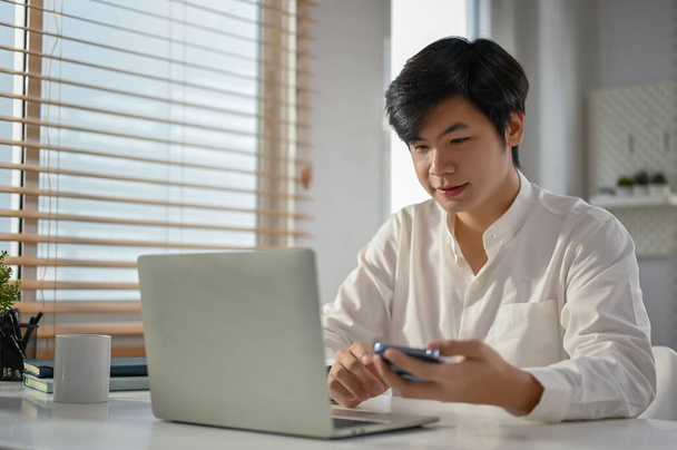 Вдохновленный и умный азиатский бизнесмен тысячелетия смотрит на экран своего ноутбука, работает над своим бизнес-проектом в офисе. - Фото, изображение