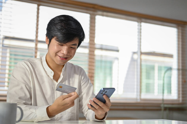 Heureux et beau millénaire homme asiatique en utilisant l'application bancaire mobile pour transférer de l'argent ou payer des factures en ligne. - Photo, image