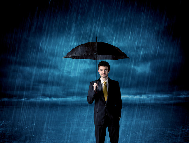 Business man standing in rain with an umbrella - Foto, Bild