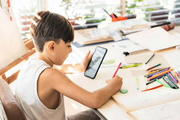 Ein Junge lernt mit seinem Smartphone zeichnen. Online-Bildung. Konzept von Technologie und Lernen. - Foto, Bild