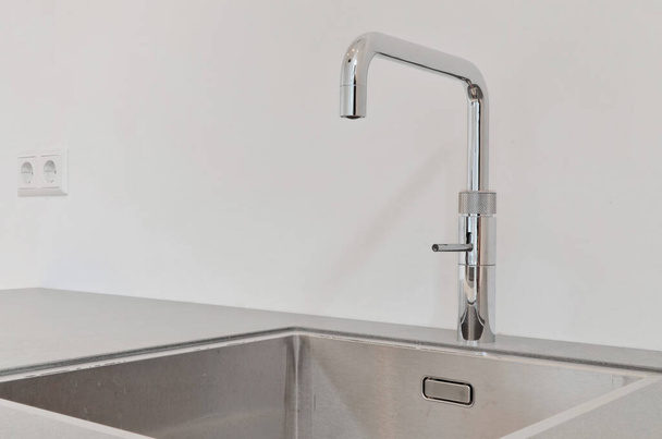 a kitchen sink with the faucet on its left side, and an empty wall in the background - Foto, imagen