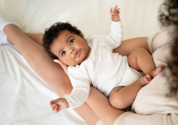 Loving young african american lady holding cute baby in her arms, enjoy tender moment on bed in light bedroom interior, top view. Family love, mother and child at home, baby care - Fotoğraf, Görsel