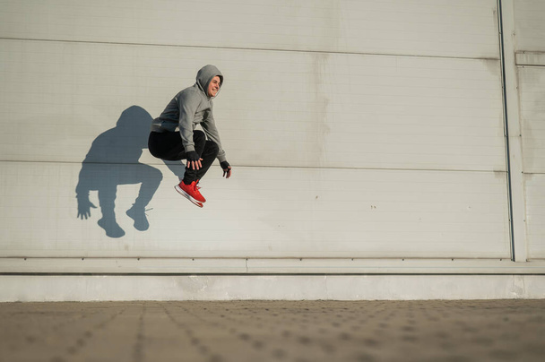 Белый мужчина в толстовке прыгает высоко с руками на коленях на улице - Фото, изображение