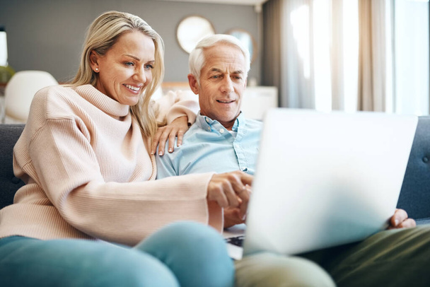 Wir bleiben gerne relevant, indem wir prüfen, was online neu ist. Ältere Paare mit einem Laptop auf dem Sofa zu Hause - Foto, Bild
