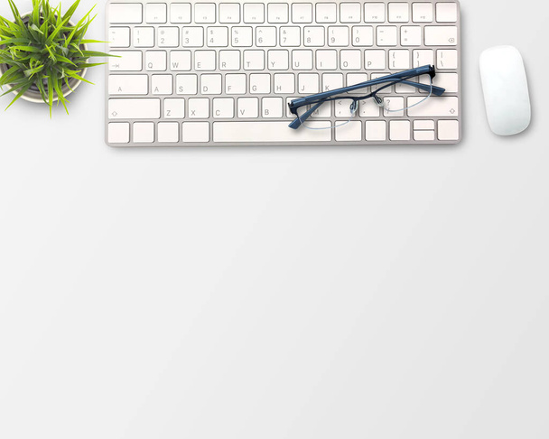 flat lay Blank notebook, computer toetsenbord, koffie, glazen en andere kantoorapparatuur op wit bureau. Bovenaanzicht met kopieerruimte.  - Foto, afbeelding
