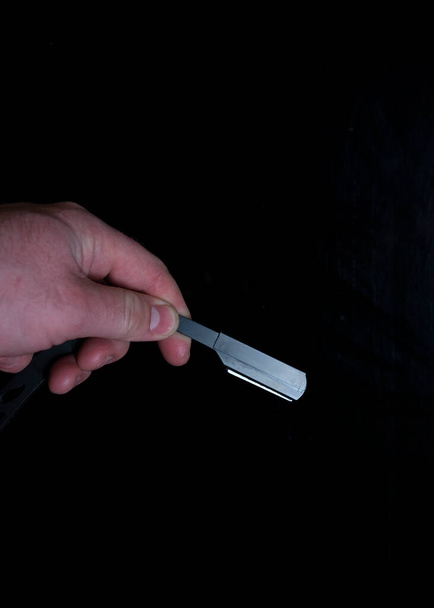 επικίνδυνο ξυράφι στο χέρι σε μαύρο φόντο - Φωτογραφία, εικόνα
