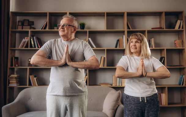 Senior couple is doing fitness training at home. Doing yoga together. Healthy lifestyle concept - Photo, Image