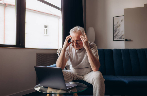 Älterer Mann mit Kopfschmerzen und Berührung des Kopfes, während er an Migräne im Wohnzimmer leidet, Älterer Mann drückt eine Hand auf den Kopf leidet unter unerträglichen Schmerzen. - Foto, Bild