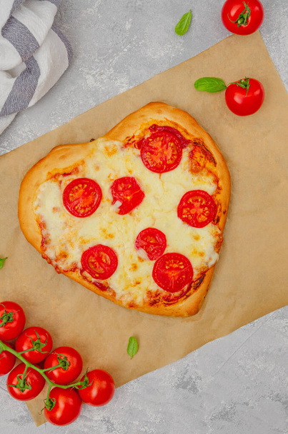 Pizza Margherita shaped heart with cherry tomatoes, mozzarella and basil on a gray concrete background. Food concept for Valentine's Day. Copy space - Fotoğraf, Görsel