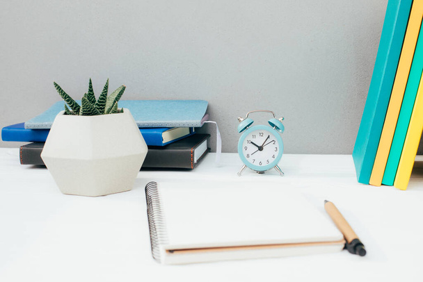 Werkplaats met briefpapier. Veelkleurige notitieblokken, blauwe wekker, sappig op een witte houten tafel tegen een grijze muur. Vooraanzicht - Foto, afbeelding