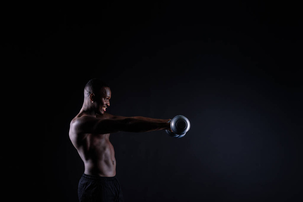 Ein junger muskulöser Mann mit afrikanischer Statur steht oben ohne auf schwarzem Hintergrund - Foto, Bild