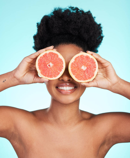Black woman, face and hands with grapefruit for skincare nutrition, beauty or vitamin C against a blue studio background. Portrait of African female smiling with fruit for natural health and wellness. - Фото, изображение