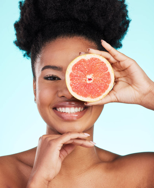 青いスタジオの背景に対してスキンケア栄養、美しさやビタミンCのための黒い女性、顔とグレープフルーツ。自然の健康と健康のための果物とアフリカ系アメリカ人女性の笑顔の肖像. - 写真・画像
