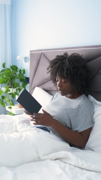 Afričanky mladá žena čtení knihy, zatímco někdo jí volat na telefonu v posteli v dopoledních hodinách. - Záběry, video