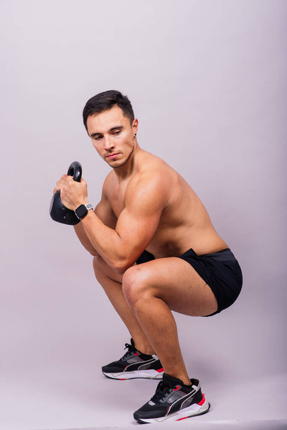 Strong young muscular focused fit man with a big muscles holding heavy kettlebells - Foto, afbeelding