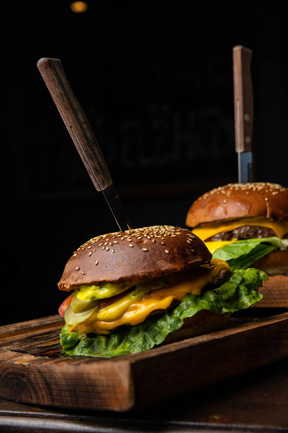 Two burgers on a wooden board with a knife and fork on it - Fotografie, Obrázek