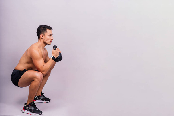 Silný mladý svalnatý soustředěný fit muž s velkými svaly drží těžké kettlebells - Fotografie, Obrázek
