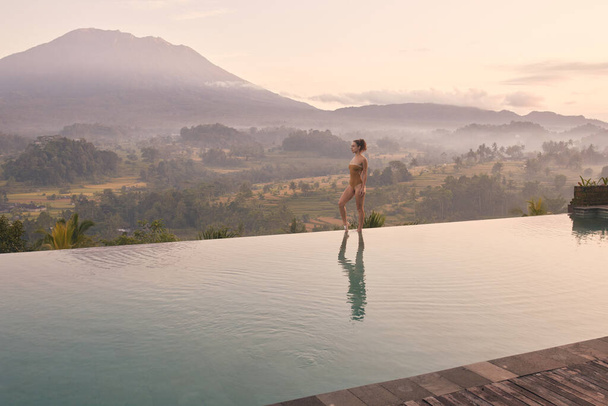 Woman Relaxing In Swimming Pool Water at Mountains. Slim Female Model Posing at Summer Travel Vacation With Volcanic View. Summertime Recreation, Relax And Spa Concept  - Foto, imagen