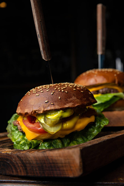 Two burgers on a wooden board with a knife and fork on it - Fotoğraf, Görsel