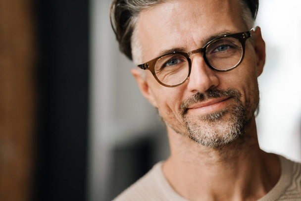 Closeup of white middle-aged man in eyeglasses smiling at camera while standing indoors - Fotoğraf, Görsel