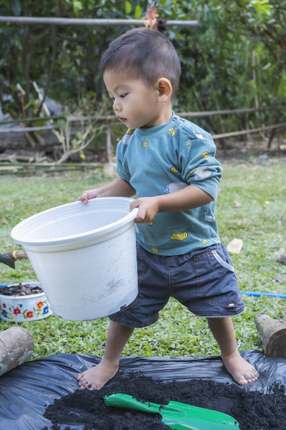 Little child holding pot to prepare plants for planting. Toddler boy standing to prepare to plant to Mother's little helper. Gardening. Hobbies at home horticulture. Leisure activities family concept - Foto, Bild