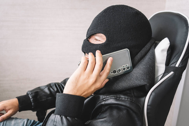 Robber making phone gesture. The concept of telephone terrorism and fraud. A masked man makes a phone call. - Photo, Image