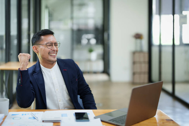 Ritratto di un imprenditore asiatico maschio in piedi con un computer che mostra felicità dopo un investimento di successo. - Foto, immagini