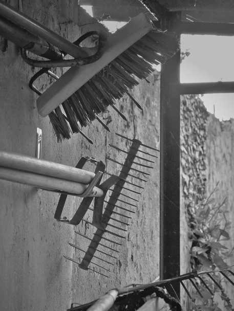 Black and white view of gardening tools hung and stored on a concrete wall, in a shed. - Photo, Image