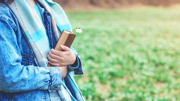 Young woman with book on the walk. Time for reading. Reading book concept. Woman enjoying spring day at nature. Lifestyle, people and spring time. - Фото, изображение