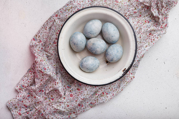 青い花と紫のキッチンテーブルの上に白いボウルにイースターの卵を描いた。トップビュー、コピースペース - 写真・画像