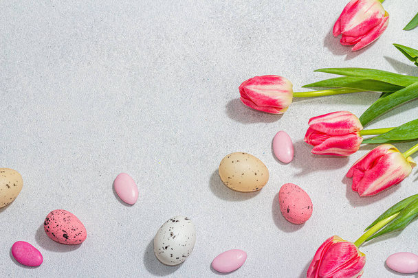 Pink tulips with Easter eggs on light stone concrete background. Festive concept, greeting card, flat lay, hard light, dark shadow, top view - Fotografie, Obrázek