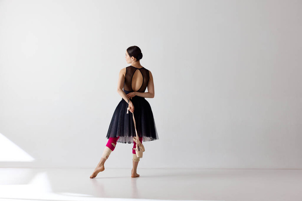 Klassischer Tänzer. Junge und anmutige Balletttänzerin in schwarzem Kleid posiert und hält Spitzenschuhe vor weißem Hintergrund in der Hand. Schönheit und Anmut. Kunst, Künstler, Bewegung, Performance-Konzept - Foto, Bild