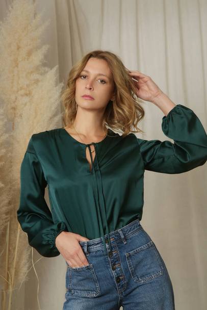 Serie of studio photos of young female model in pine green silk blouse and relaxed jeans - Photo, image