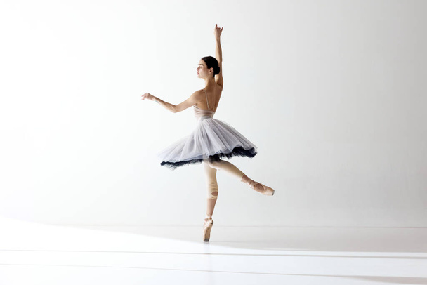 Mostrando flexibilidade e graça. Bailarina vestindo tutu dançando movimentos elegantes sobre fundo branco. Beleza da dança clássica. Conceito de balé clássico, inspiração, beleza, dança, criatividade - Foto, Imagem