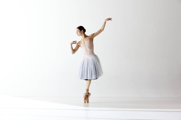Solo performance. Ballerina dancing graceful movement in dress over white background. Art, motion, action, flexibility, inspiration concept. Beauty of contemporary dance - Fotó, kép