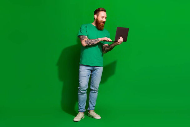Full length photo of funky cool man wear t-shirt typing emails modern gadget isolated green color background. - Foto, Imagen