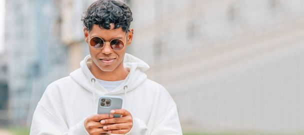 mladý muž ve slunečních brýlích při pohledu na mobilní telefon na ulici - Fotografie, Obrázek