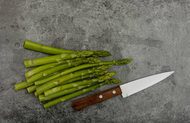 Primo piano mazzo di asparagi verdi freschi e coltello sul tagliere o sulla superficie del tavolo in pietra grigia, vista dall'alto, direttamente sopra
 - Foto, immagini