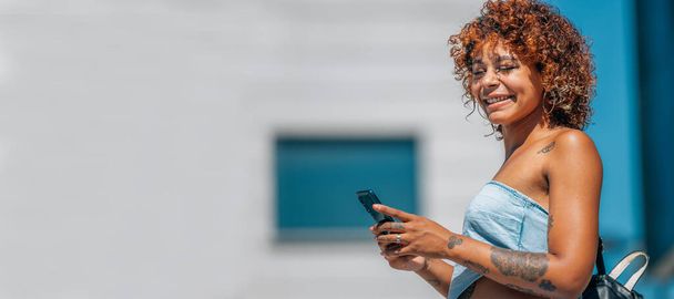 latin zwart meisje met mobiele telefoon in de straat met stedelijke stijl - Foto, afbeelding