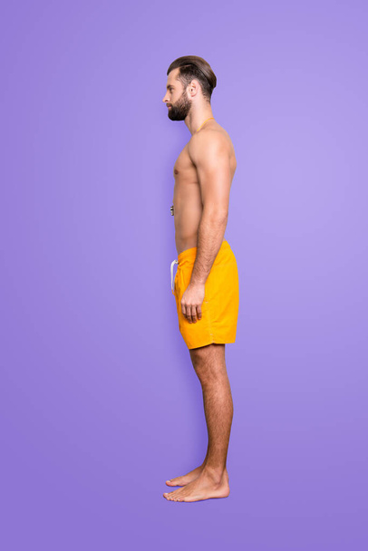 Side view snap full size fullbody portrait of attractive strong lifeguard with stubble, modern hairstyle in yellow shorts isolated on grey background. - Zdjęcie, obraz